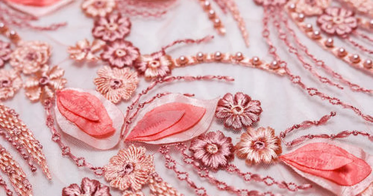 Pink and rose-gold floral appliqué with beadwork on sheer fabric, showing layered fabric shapes stitched onto the ground