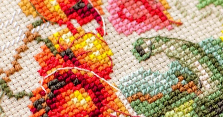 Close-up of colorful cross-stitch embroidery on Aida cloth showing autumn-toned floral motifs