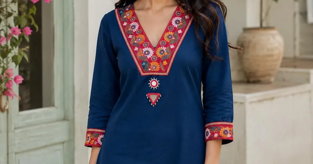 A woman wearing a teal hand-embroidered kurti with a floral stitched V-neckline and matching cuff borders