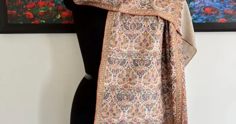 A cream embroidered shawl with intricate floral stitchwork draped over a display stand