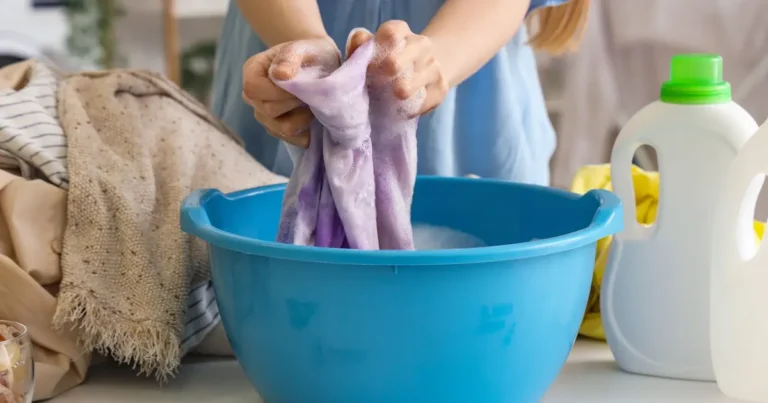 Hands gently hand-washing a stained garment in a blue basin