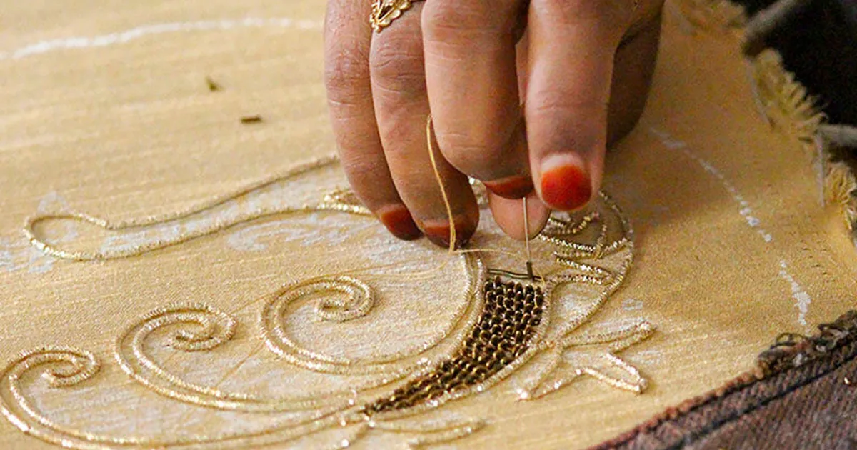 Artisan's hands working gold zardozi metal-thread embroidery on fabric, couching coiled dabka wire